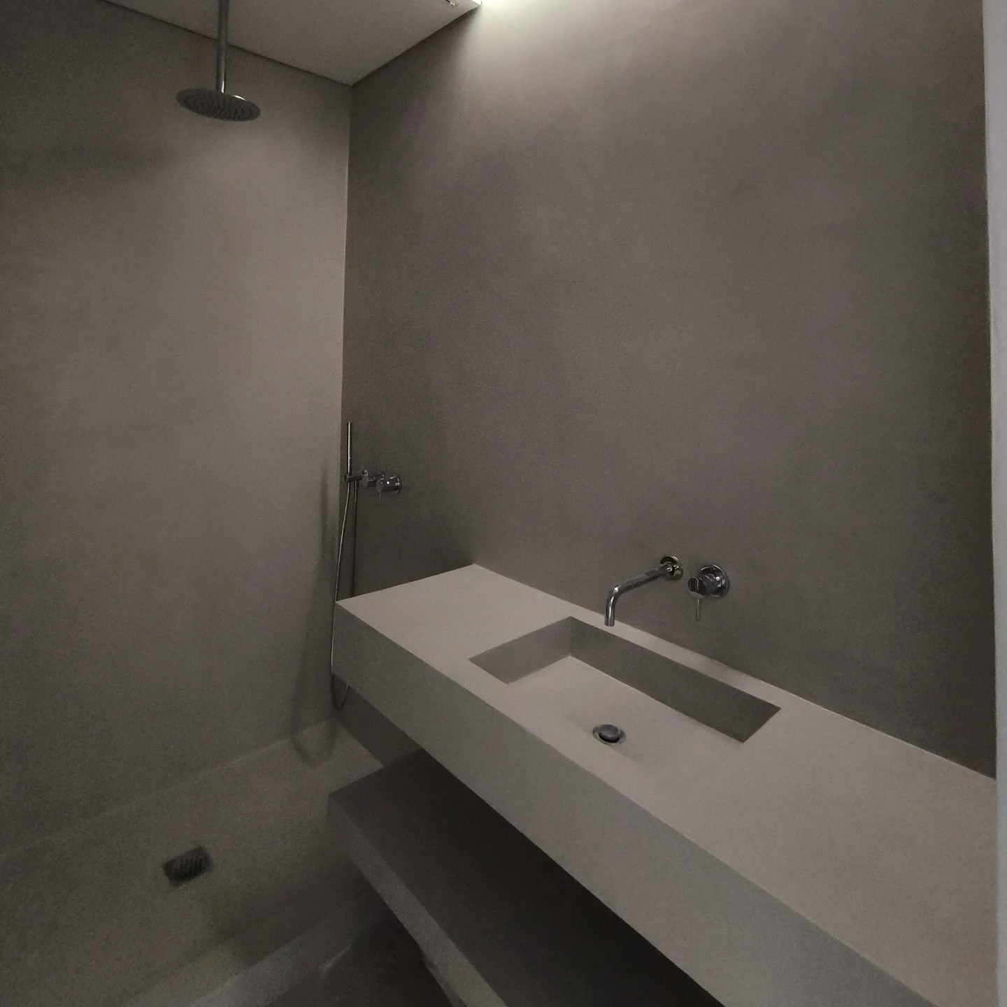 Casa de banho com superfície contínua em microcimento fosco de tom cinzento, lavatório integrado e linhas minimalistas