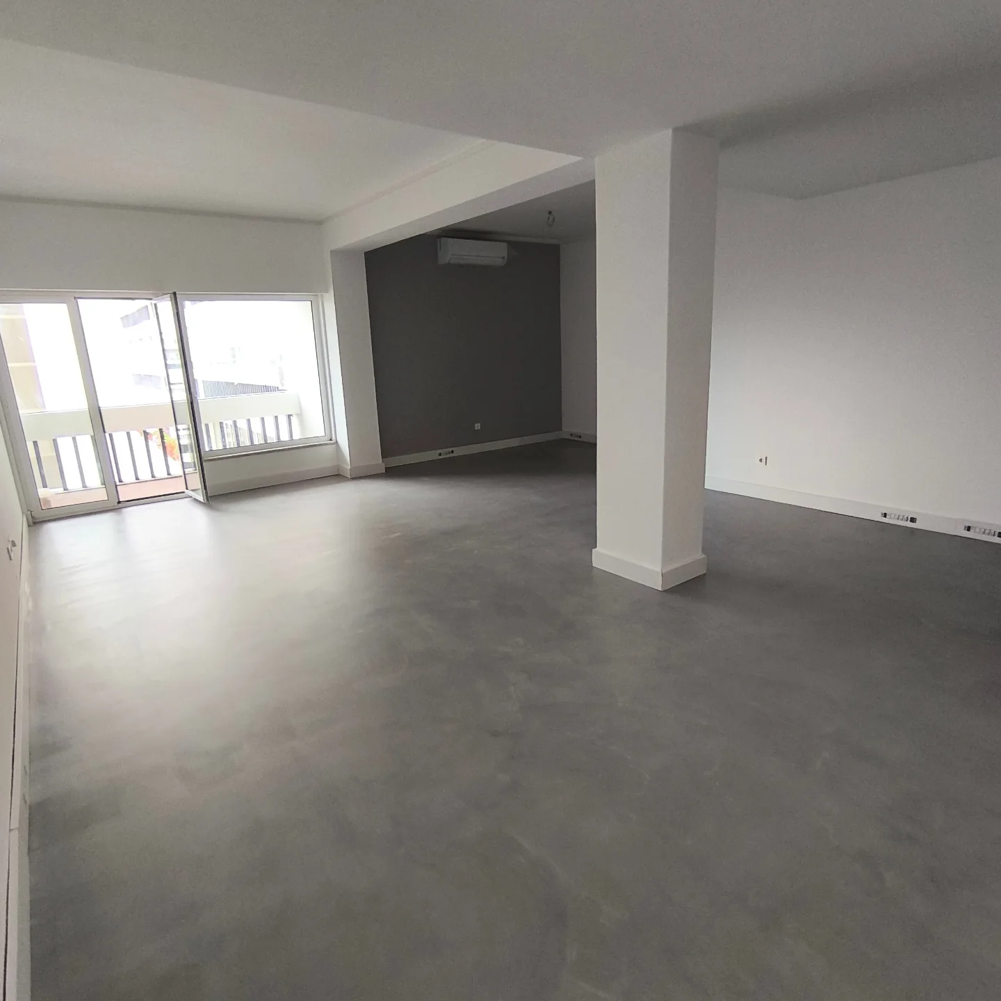 Apartamento remodelado com pavimento de efeito microcimento cinzento contínuo, paredes claras e zona de destaque mais escura